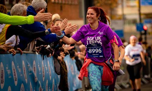 Woman giving high fives to the crowd whilst running in the ̽Ƶ Leeds Abbey Dash